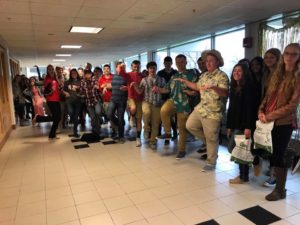 Large group of young men and women standing like flamingos, holding pink feather pins