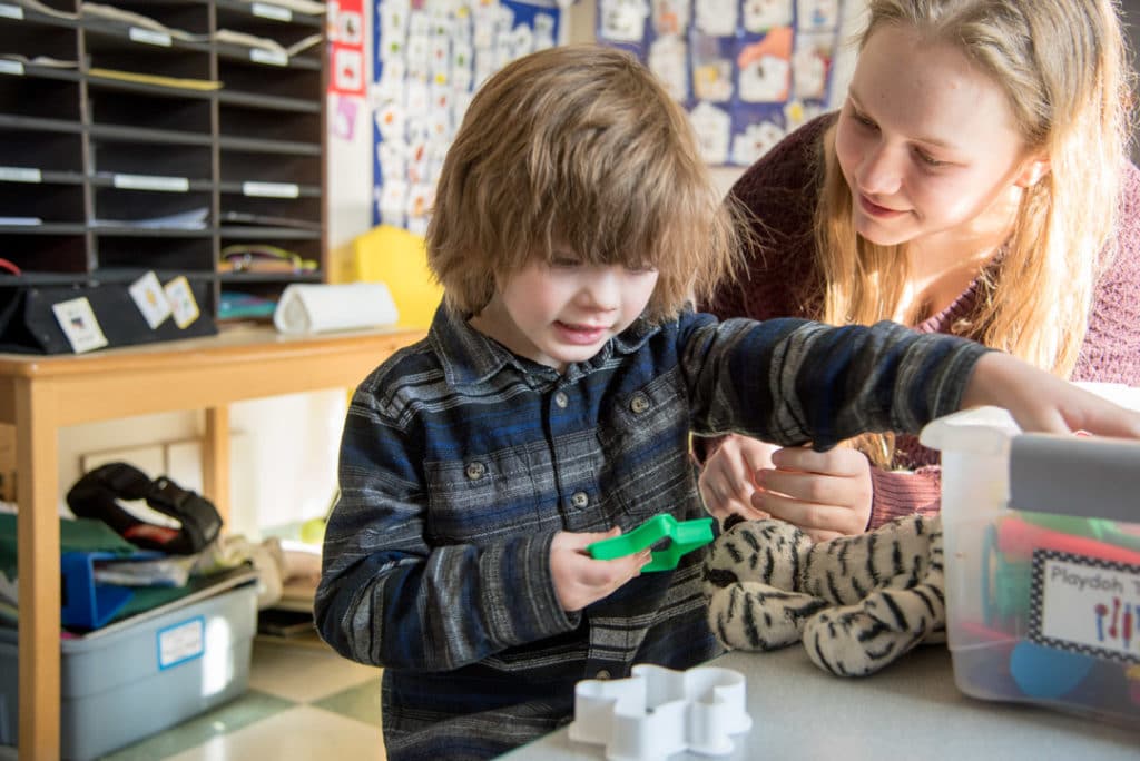 Child playing with a playdoh cookie cutter while caretaker watches